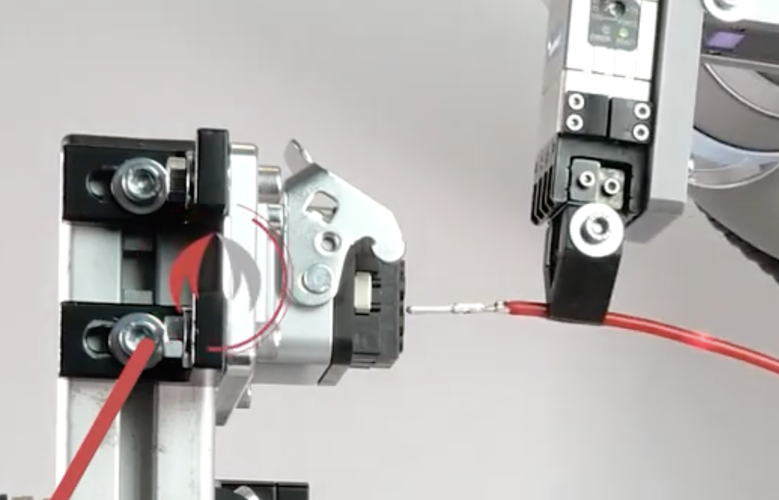 Robot gripper guiding a red wire toward an electrical terminal