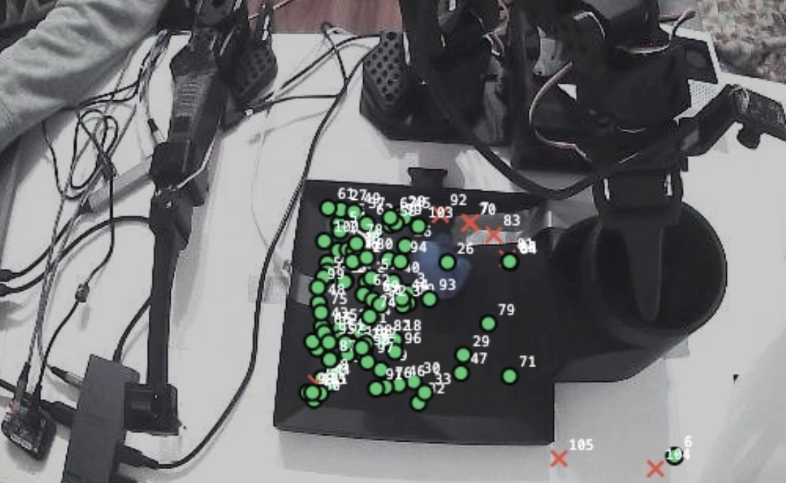 Camera view of the eval workspace with rollout outcomes overlaid: green dots mark successful attempts, red X marks failures